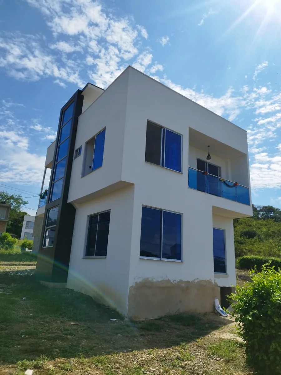 Casa de dos pisos con ventanales azules y baranda de vidrio