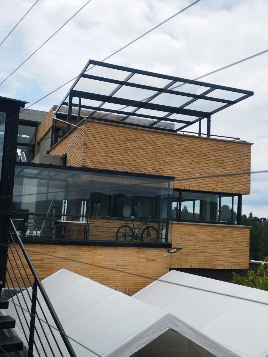 Marquesina de vidrio con estructura negra sobre una terraza