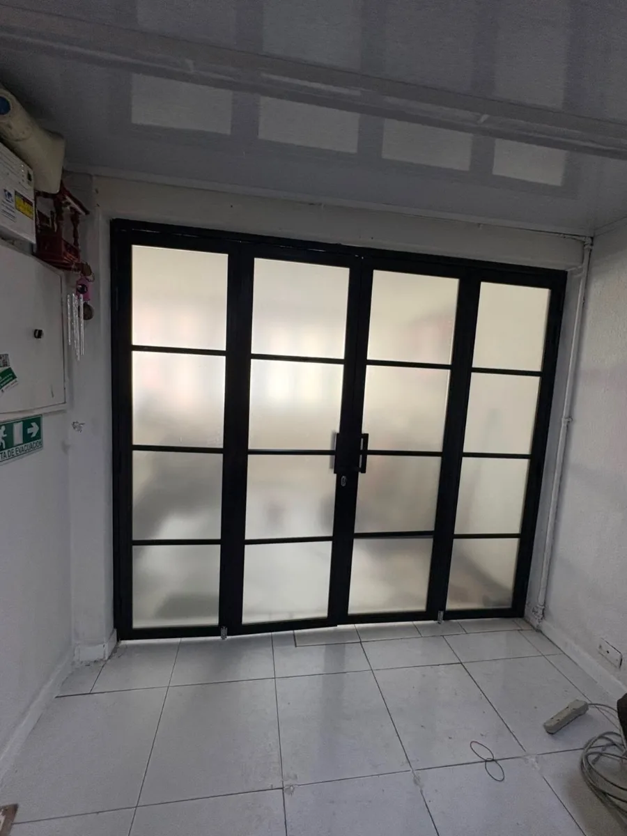 Puerta en acordeón de aluminio negro con vidrio esmerilado