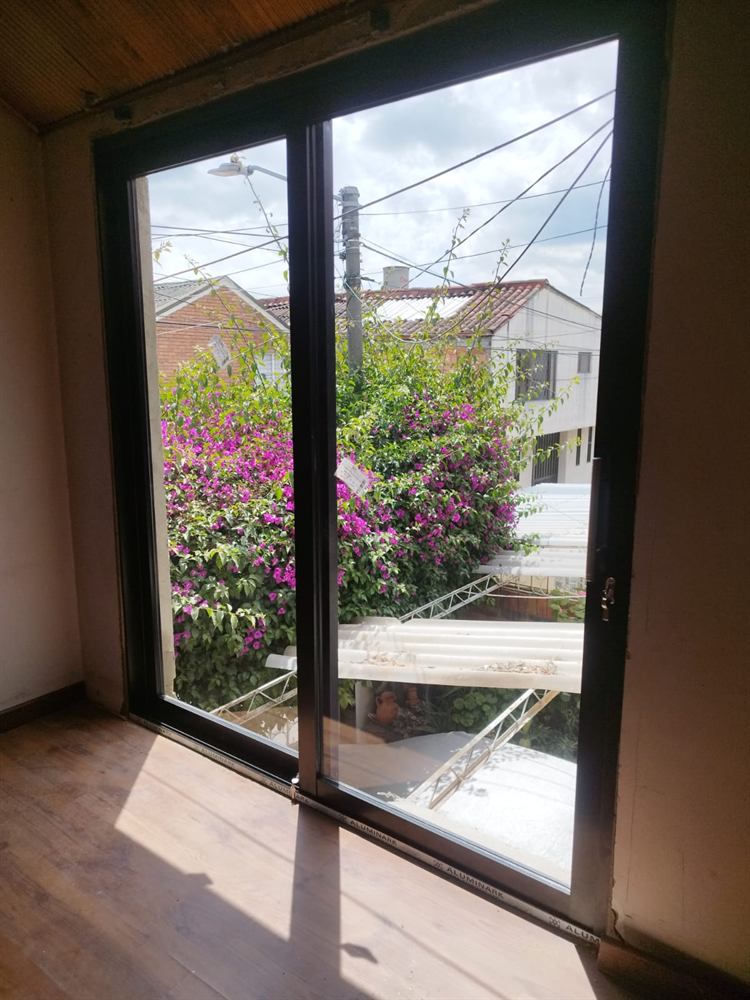 Puerta-ventana corrediza de aluminio negro que da a un jardín con buganvilias